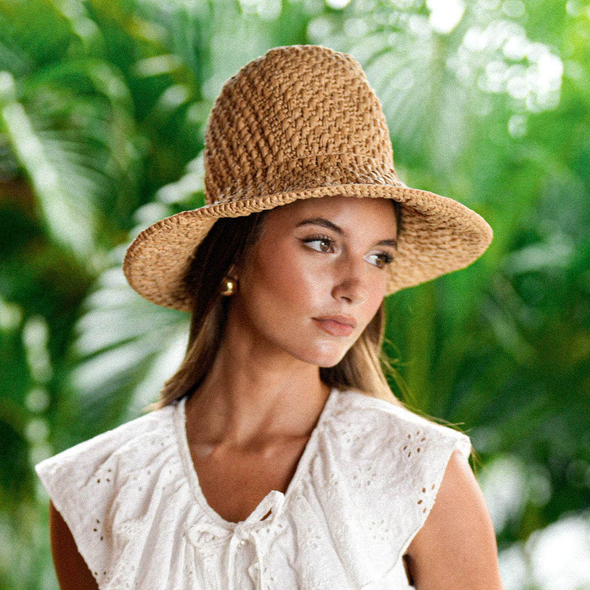 A Woman, Rachelle Van Waardhuizen is wearing BrunnaCo's artisanal Nina raffia straw hat and white Padar embroidery dress with a blurred green background of a lush tropical jungle in Bali