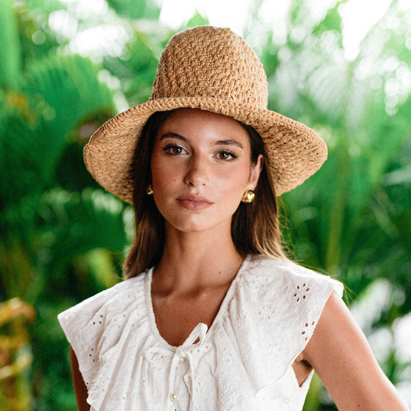 A Woman, Rachelle Van Waardhuizen is wearing BrunnaCo's artisanal Nina raffia straw hat and white Padar embroidery dress with a blurred green background of a lush tropical jungle in Bali