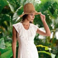 A Woman, Rachelle Van Waardhuizen is wearing BrunnaCo's artisanal Nina raffia straw hat and white Padar embroidery dress with a blurred green background of a lush tropical jungle in Bali