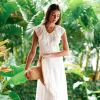 A Woman, Rachelle Van Waardhuizen is wearing BrunnaCo's artisanal Nina raffia straw hat and white Padar embroidery dress with a blurred green background of a lush tropical jungle in Bali