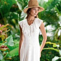 Woman in a white vacation dress and straw hat standing in a tropical setting