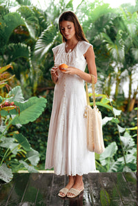 Woman in a white embroidered vacation summer dress holding an orange in a tropical setting