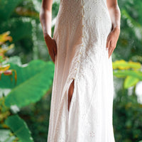 White lace vacation dress with a slit in front, worn by a person, against a green leafy background.