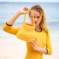 Olga is strolling by the shore with BrunnaCo's Petite Naga Macrame Beach Bag in Butter Yellow — the perfect companion for a sun-kissed summer day.