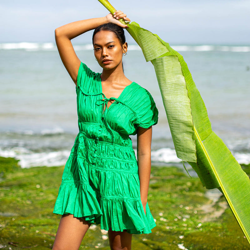 A woman is wearing SRIKANDI Ruffle Cotton Dress In Kelly Green at the tropical beach in Cannes, France Bingin Bali
