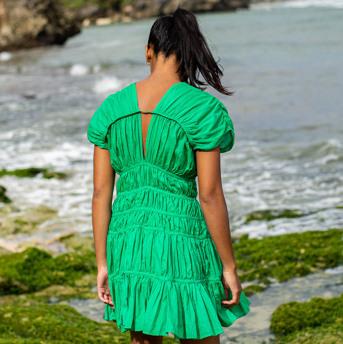 A woman is wearing SRIKANDI Ruffle Cotton Dress In Kelly Green at the tropical beach in Cannes, France Bingin Bali