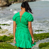 A woman is wearing SRIKANDI Ruffle Cotton Dress In Kelly Green at the tropical beach in Cannes, France Bingin Bali