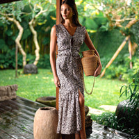 Floral cotton Black Cherry midi dress with ruffle trim and slit, handcrafted by artisans, paired with a woven rattan bag with gold chain—sustainable resortwear and women’s fashion by BrunnaCo