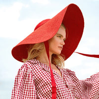 BrunnaCo Lola Wide Brim Jute Straw Hat in Red. A wide-brimmed straw hat in a vibrant red color. The hat is made from natural jute fibers and features a comfortable inner lining. It is perfect for sun protection and style. Handmade by women artisans in Bali, Indonesia