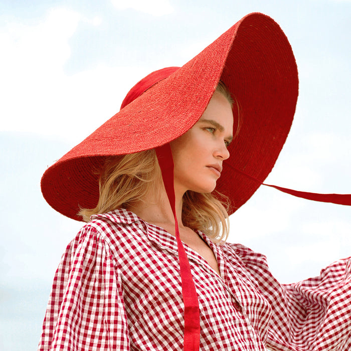 BrunnaCo Lola Wide Brim Jute Straw Hat in Red. A wide-brimmed straw hat in a vibrant red color. The hat is made from natural jute fibers and features a comfortable inner lining. It is perfect for sun protection and style. Handmade by women artisans in Bali, Indonesia