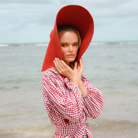 BrunnaCo Lola Wide Brim Jute Straw Hat in Red. A wide-brimmed straw hat in a vibrant red color. The hat is made from natural jute fibers and features a comfortable inner lining. It is perfect for sun protection and style. Handmade by women artisans in Bali, Indonesia