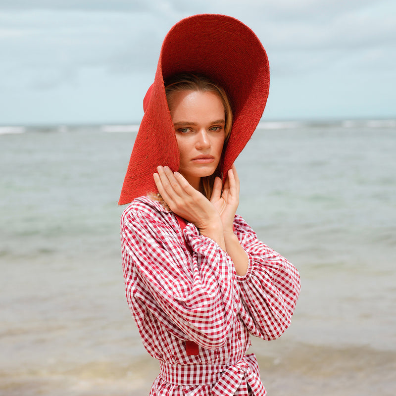 BrunnaCo Lola Wide Brim Jute Straw Hat in Red. A wide-brimmed straw hat in a vibrant red color. The hat is made from natural jute fibers and features a comfortable inner lining. It is perfect for sun protection and style. Handmade by women artisans in Bali, Indonesia
