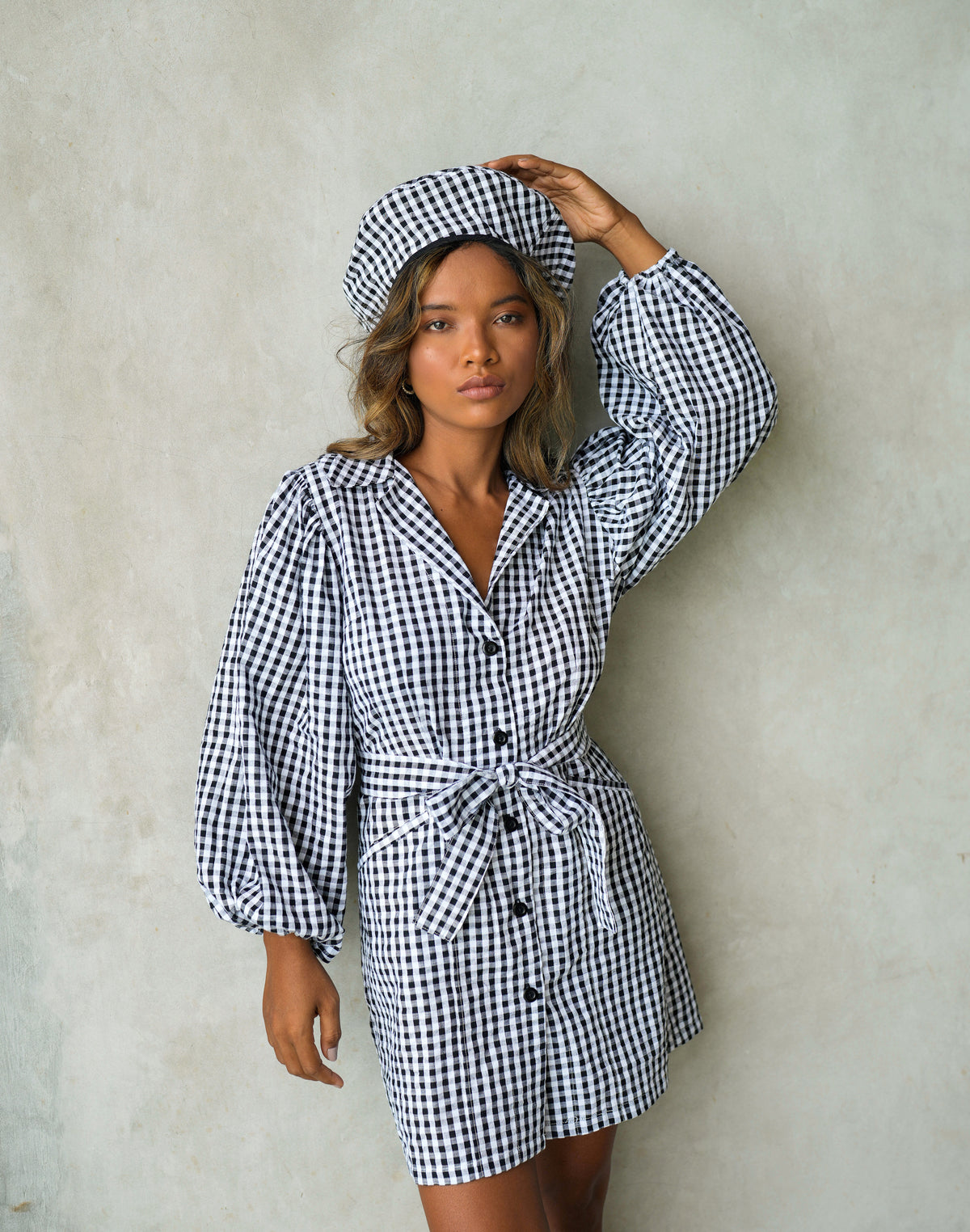 BrunnaCo Meghan Mini Gingham Dress in Black - A stylish and versatile dress made from 100% cotton. This dress features a sweet silhouette with voluminous medium-length puff sleeves, a chic short skirt with bow-detailing, and a removable waist belt. The Meghan Mini Gingham Dress is perfect for any occasion, from a casual picnic to a formal event.