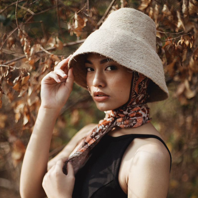 Naomi Jute Straw hat in Beige. Naomi Jute Bucket Hat is designed specifically for the wild at heart with classic sophistication. Enjoy lounging poolside or exploring the city on sun-soaked days as its protective hat brim provides ample shade. Made of natural jute straws which have the perfect weight, this hat will sit comfortably and won't fly away in sudden gusts. It's also very practical to pack in any size luggages and ideal to take on any trips.