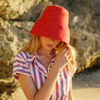 Naomi Jute Bucket Hat in red is designed specifically for the wild at heart with classic sophistication. Enjoy lounging poolside or exploring the city on sun-soaked days as its protective hat brim provides ample shade. Made of natural jute straws which have the perfect weight, this hat will sit comfortably and won't fly away in sudden gusts. It's also very practical to pack in any size luggages and ideal to take on any trips.