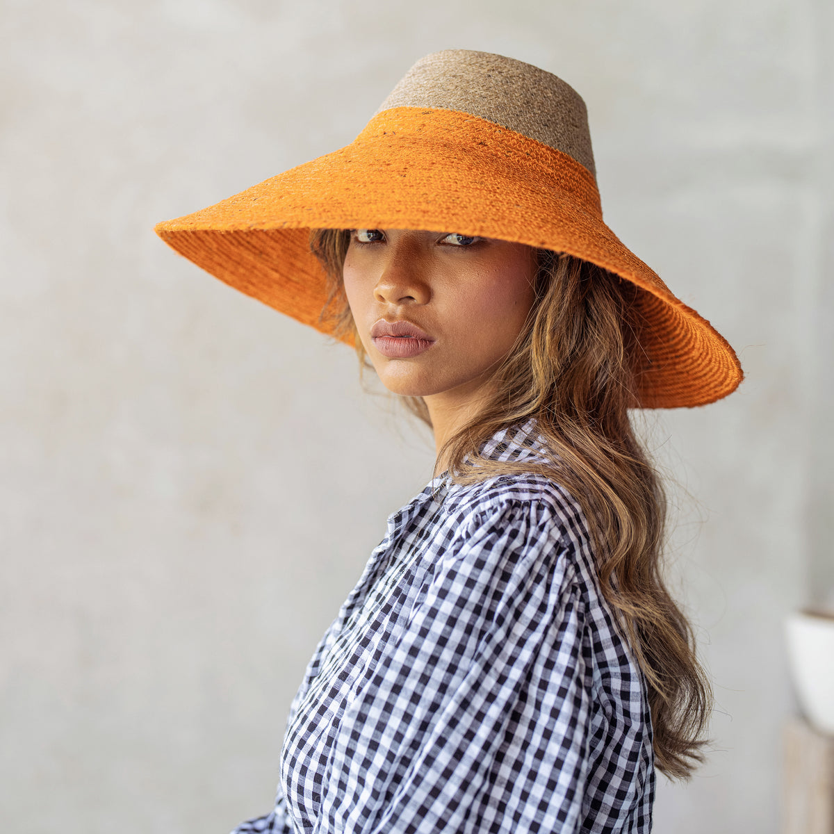 Duo color tone handwoven beach straw hat in natural and pumpkin orange color, handmade from natural jute straw by local artisan in Bali. Handmade vacation wide-brim hat with domed down brim for maximum sun protection. Sustainably made by female artisan community in Indonesia for resort vacation season.
